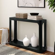 a black table with two white vases on it in front of a framed painting