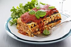 a white plate topped with lasagna covered in sauce and garnished with green leaves