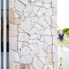 a woman walking past a stone wall with flowers growing on it and the door open