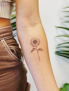 a woman's arm with a small sunflower tattoo on the left inner arm