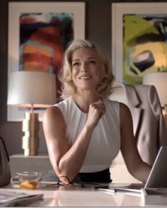 a woman sitting at a desk with a laptop computer in front of her, smiling