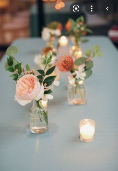 several vases with flowers and candles on a blue table cloth covered table in an indoor setting