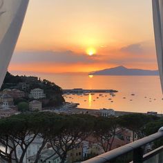 the sun is setting over an ocean with boats in the water and buildings on the shore