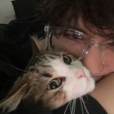 a woman wearing glasses holding a cat with her face close to it's chest