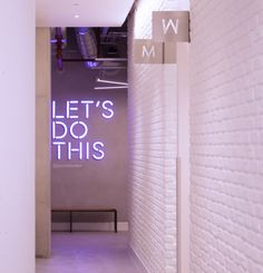 the entrance to an office building with white brick walls and purple neon letters on the wall