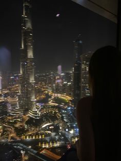 a woman is looking out at the city lights and skyscrapers from an observation platform