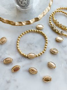 gold beaded bracelets and rings sitting on a marble table next to a bottle of water