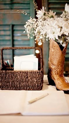 a brown cowboy boot next to a basket with white flowers in it on a table