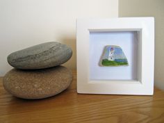 two rocks sitting on top of a wooden table next to a white frame with a lighthouse