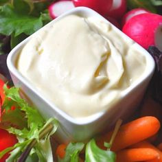 a bowl of dip surrounded by carrots and radishes