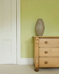 a wooden dresser sitting next to a green wall with a vase on top of it