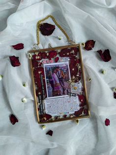 a photo frame hanging on a white sheet with rose petals around it and a gold chain