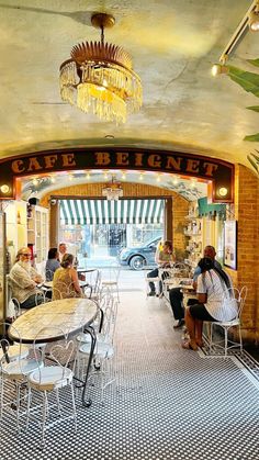 people are sitting at tables in an old fashioned cafe with chandelier above them