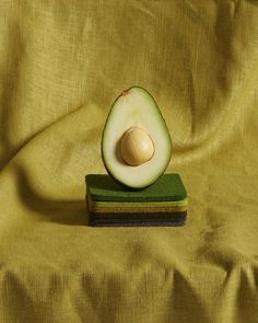 an avocado cut in half sitting on top of a green block of cloth