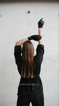 a woman wearing black gloves and holding her hands up in the air while standing against a white wall