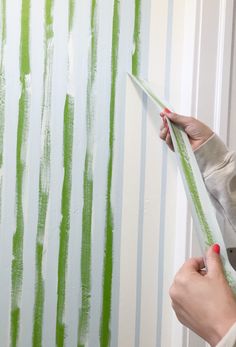 a woman is painting a wall with green stripes on it and holding a pair of scissors in her hand