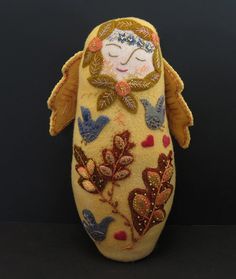 an embroidered doll with leaves and birds on it's body, sitting in front of a black background