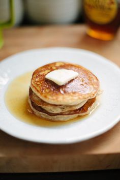 a stack of pancakes on a white plate with butter and syrup drizzled on top