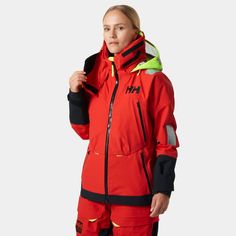 a woman wearing a red and black ski suit with yellow accents on the hood, standing in front of a white background