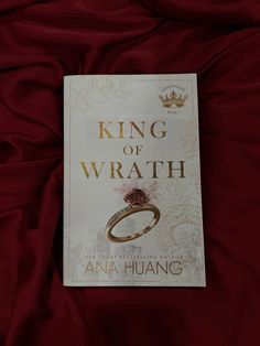 a book sitting on top of a bed covered in red sheets and a gold ring