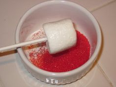 a white bowl filled with red liquid and a marshmallow stick sticking out of it