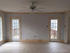 an empty living room with wood paneling and two doors leading to the deck area