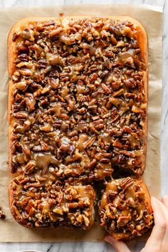 pecan nut bread on parchment paper with two hands reaching for the top and one hand holding an uncooked loaf