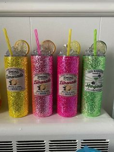 four different colored tumblers with lemon slices and straws in them sitting on a shelf