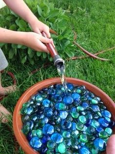 a person is pouring water into a bowl filled with blue glass pebbles in the grass