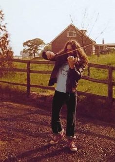 a woman is playing violin in front of a wooden fence and farm house on a sunny day