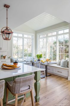 a kitchen with white cabinets and green island in front of two windows that look out onto the woods