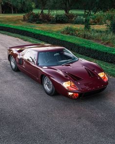 a red sports car parked on the side of a road next to bushes and trees