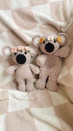 two crocheted teddy bears with flowers on their heads are sitting on a blanket