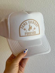 a person holding up a white hat with the words same cowboy forever on it in gold lettering