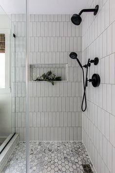 a white tiled shower with black fixtures and plants in the window box on the wall