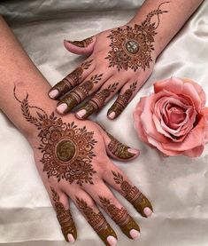 two hands with henna designs on them next to a pink rose and white satin