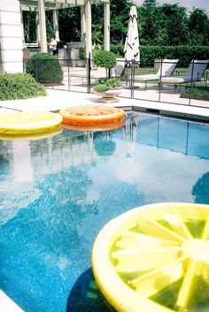 an empty swimming pool with yellow and orange floaters on it's sides, in front of a white house