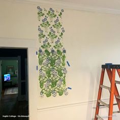 the wall is being painted with green and blue flowers on it, along with two ladders