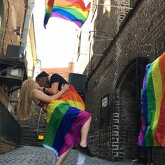 two people hugging each other in the middle of an alleyway with rainbow flags flying above them