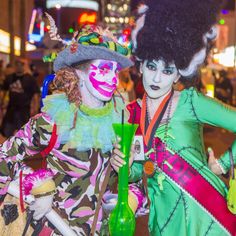 two people dressed up in costumes and makeup at an outdoor event with neon lights behind them