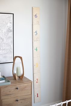 a tall growth chart next to a dresser with a candle and vase in front of it