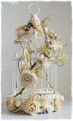 a white birdcage with flowers and ribbons on it's sides is labeled