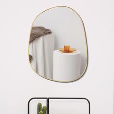 a round mirror hanging on the wall above a table with a potted cactus in it