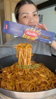 the woman is eating noodles with chopsticks in her hand while holding up a package