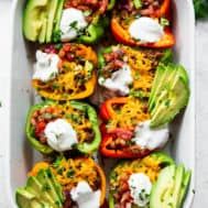 stuffed bell peppers with cheese and avocado in a casserole dish on a table