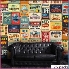 a black leather couch sitting in front of a wall covered with colorful vintage tin signs