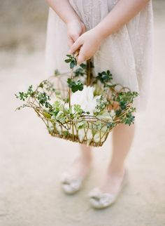 a woman holding a basket with flowers and greenery on the inside, while wearing white slippers