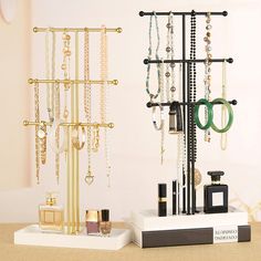 two jewelry racks with rings, bracelets and perfume bottles on them in front of a white wall