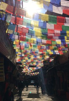 the sun shines brightly through colorful flags hanging above an alleyway in a city