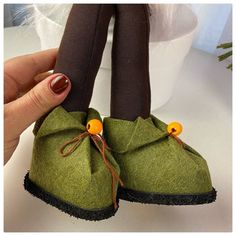 a hand holding a pair of green slippers with orange buttons on the top and bottom